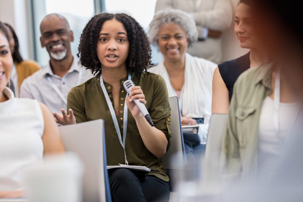 Young woman gestures while asking a question during a seminar or conference.