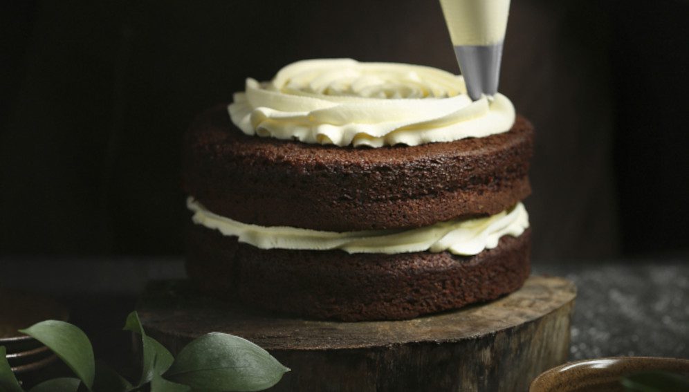 Pastry chef using icing bag to decorate chocolate cake, (public domain CC0 photo)