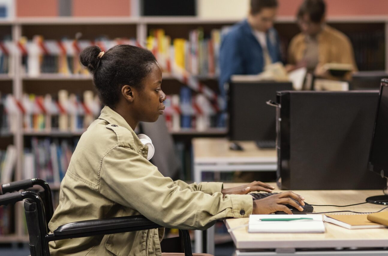 A woman in a wheelchair focused on using a computer to access the Professional Competency Framework for research managers.