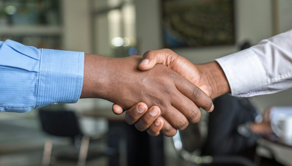 Two professionals shaking hands during a meeting, representing collaboration and partnership.